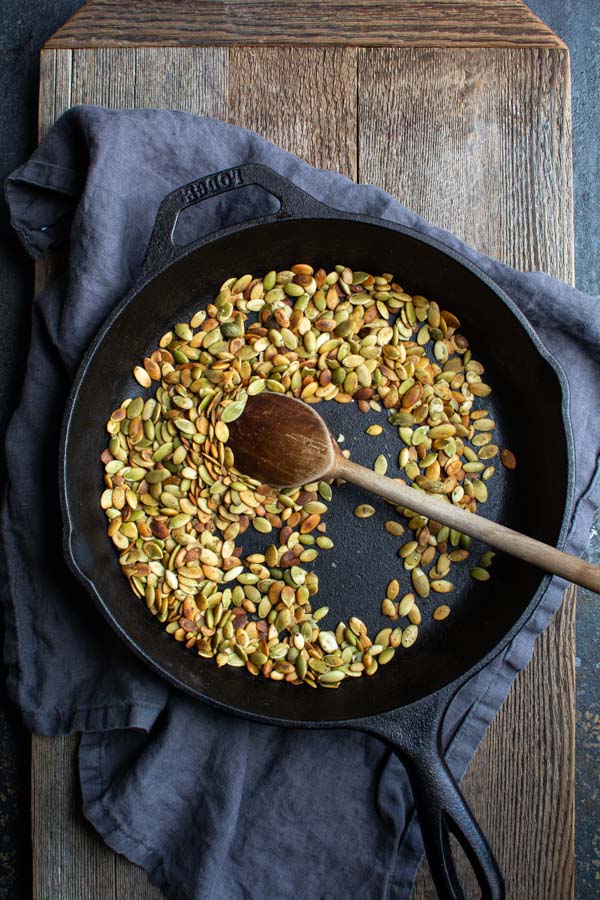 Cast iron skillet with toasted pumpkin seeds and wooden spoon