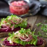 two slices bread spread with beet butter, sliced avocados, and pickled onions