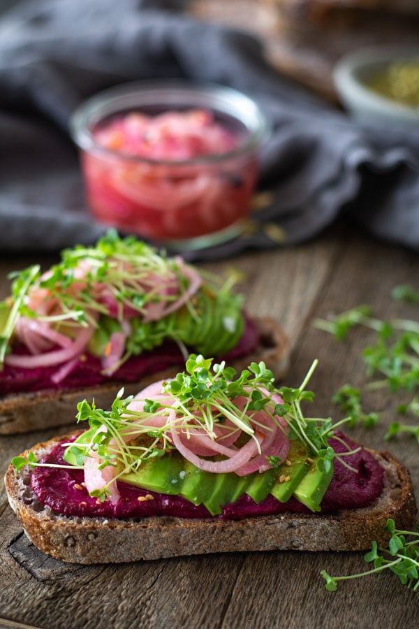 two slices bread spread with beet butter, sliced avocados, and pickled onions