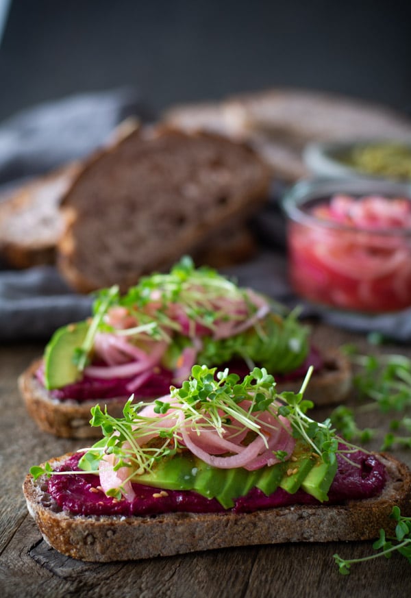 Two slices of bread layered with beet butter, avocado, pickled onions