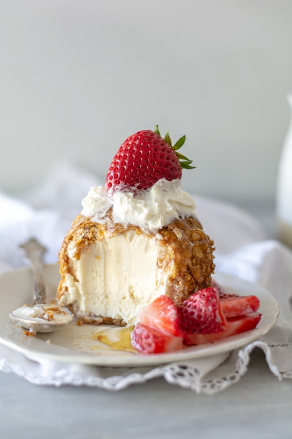 Fried ice cream with spoonful taken out with honey and berries.