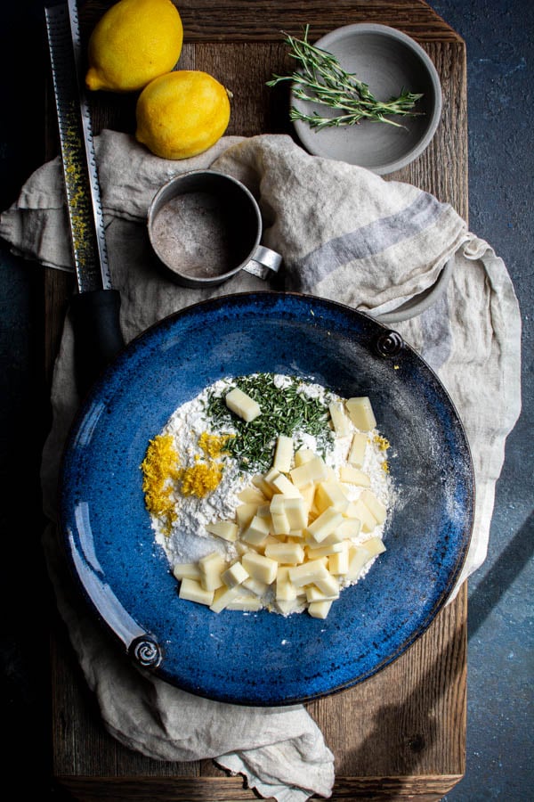 blue bowl with flour, cubed gruyere cheese, lemon zest, rosemary