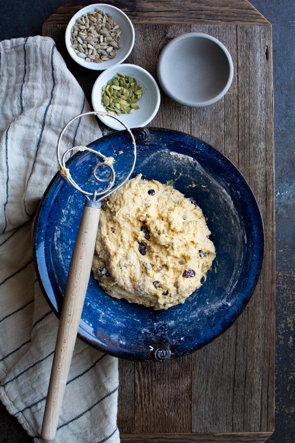 A blue bowl with pumpkin harvest bread dough and a dough whisk on the side of the bowl.
