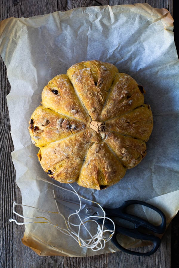 Overhead shot of baked of pumpkin bread on parchment paper with cut strings and scissors