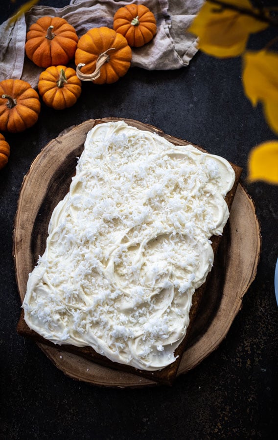 Overhead shot of pumpkin cake spread with cream cheese icing topped with flaked coconut