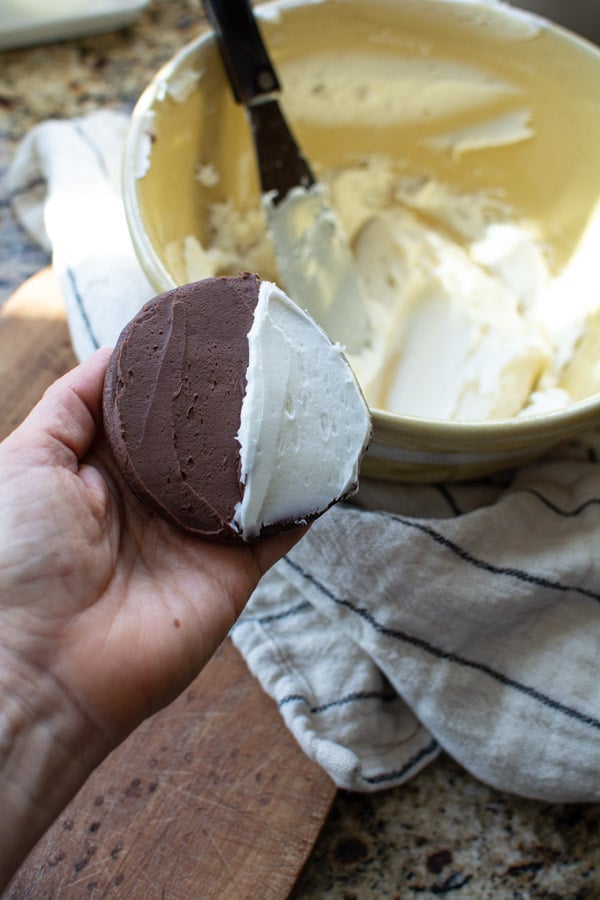 Hand holding chocolate cookie iced with chocolate and vanilla icing on each half of the cookie