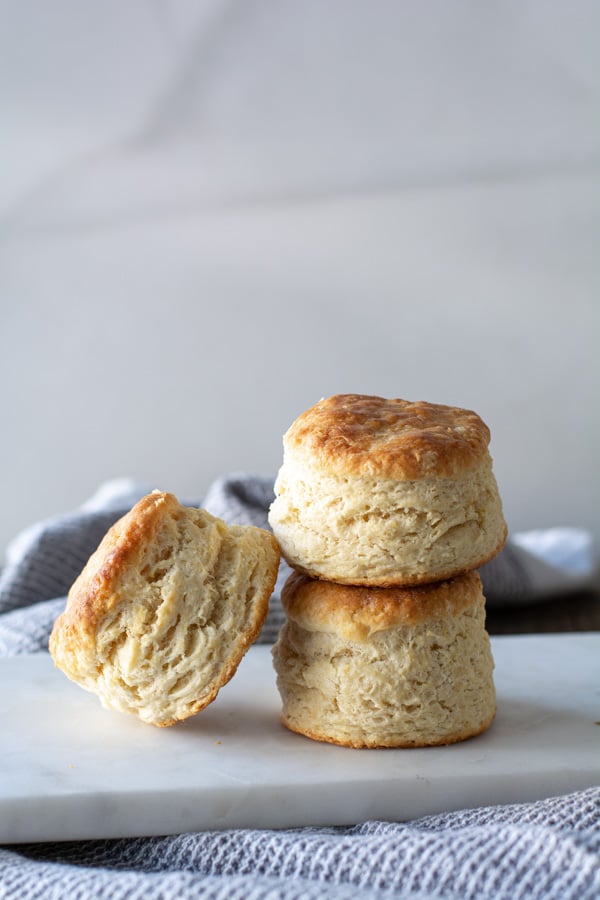 Two baked skyscraper buttermilk biscuits stacked with one biscuit leaning.