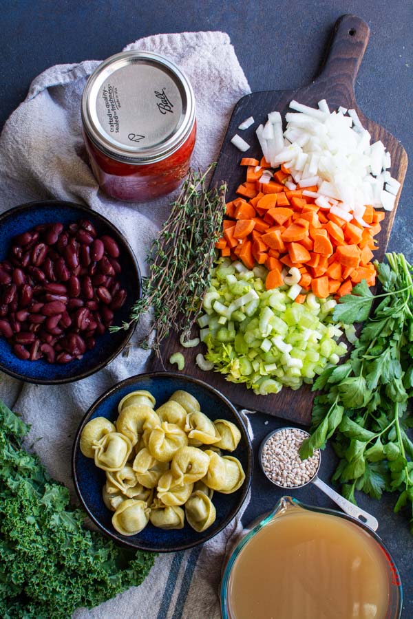 Chopped veggies, beans, tortellini, and herbs on a board