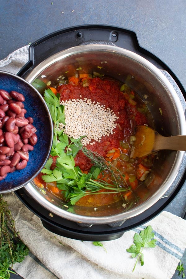 A slow cooker with sauteed vegetables, broth, barley, tomatoes and fresh herbs