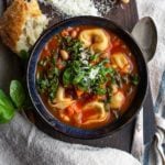 Overhead shot of minestrone soup with cheese tortellini in a bowl with a chunk of bread and fresh grated parmesan cheese.