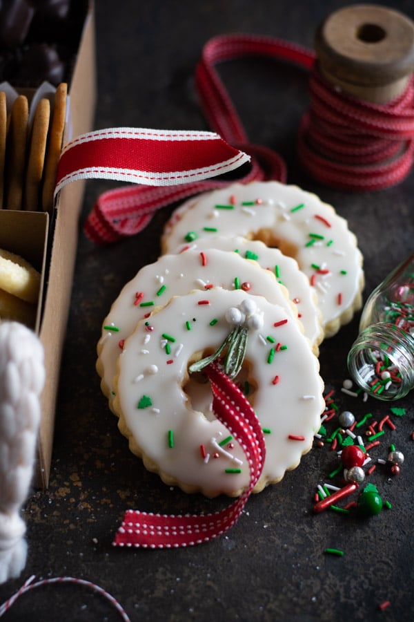 Wreath shaped iced cookies with sprinkles with a red striped ribbon through the center hole