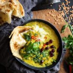 Bowl filled with coconut lentils topped with cilantro, chilis, pomegranate and paratha
