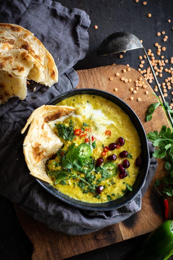 Bowl filled with coconut lentils topped with cilantro, chilis, pomegranate and paratha