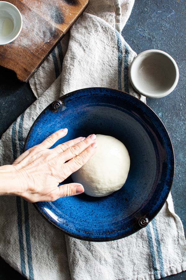 Round ball of paratha dough in a large bowl being oiled by hand