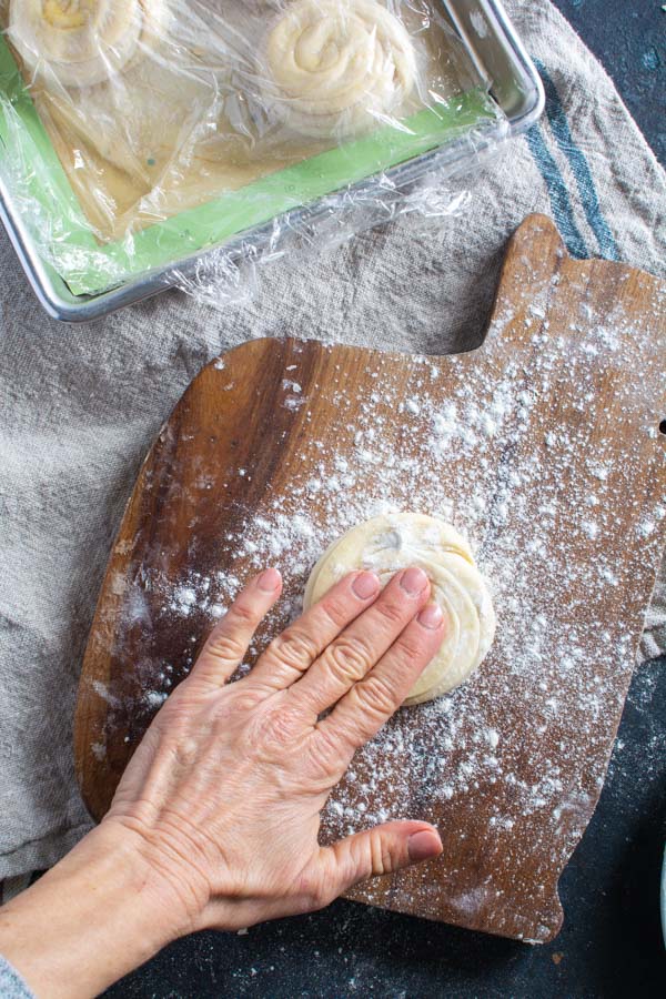 Hand pressing layered paratha dough in floured board.