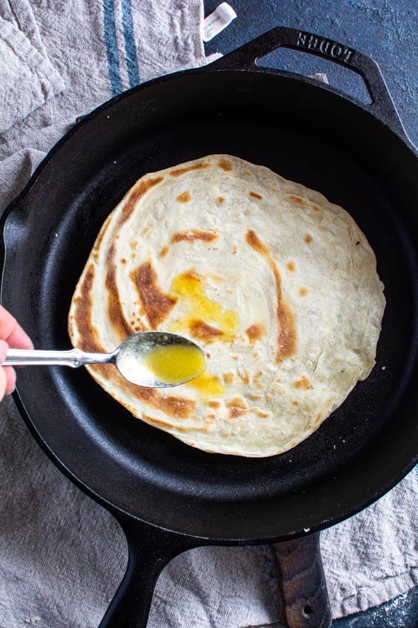 Cooked paratha in cast iron skillet with ghee drizzled on top