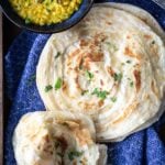 Flakey Paratha flat bread stacked on a cloth with a bowl of lentils