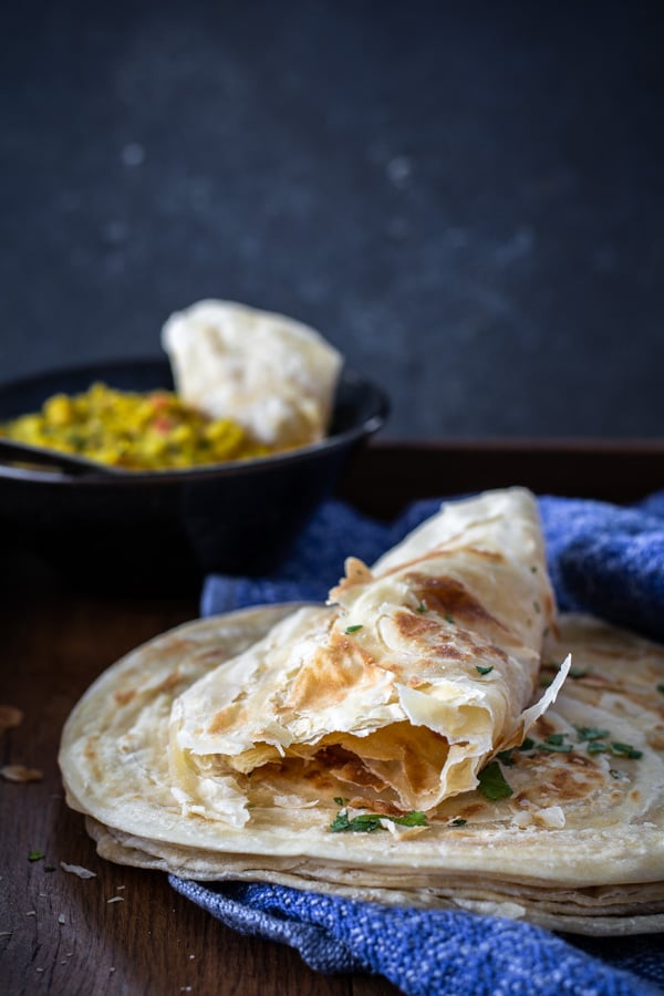 Stack of flakey paratha with bowl of lentils in background