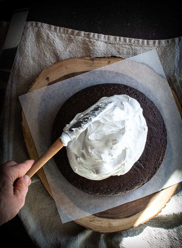 Large pile of boiling icing on top of a round devil's food cake