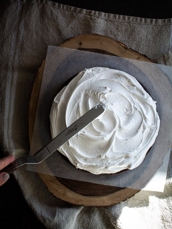 Spatula spreading boiled icing over top of chocolate cake