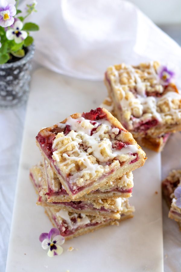 Stacked Strawberry Rhubarb Almond Crumble Bars on a white marble slab.