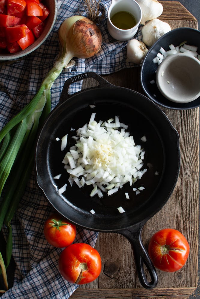 Large Cast iron skillet with chopped onions and garlic.