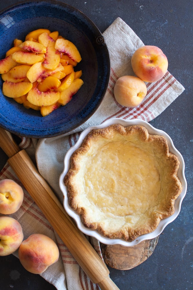 A bowl of peaches next to a baked pie shell