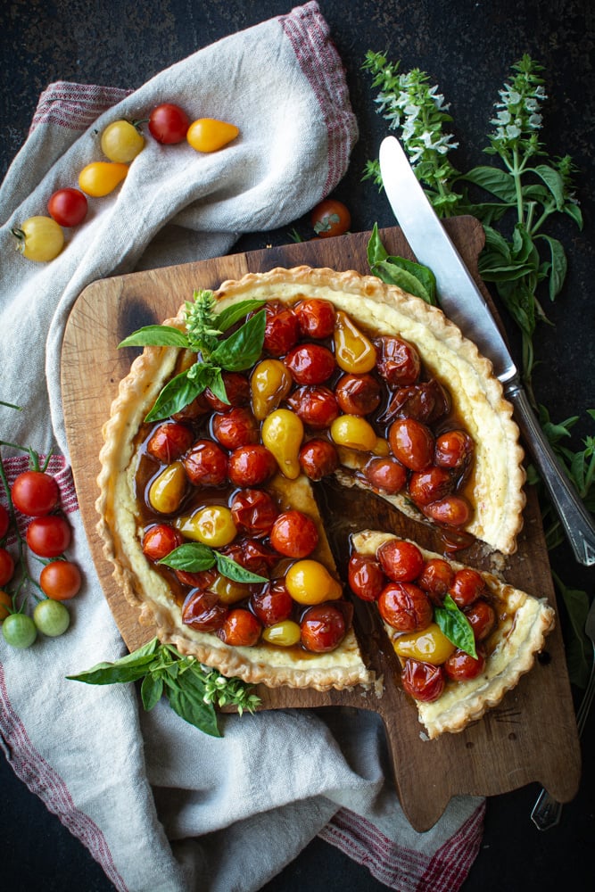 Baked ricotta tart topped with jammy cherry tomatoes with a wedge cut.