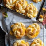 Giant cheddar twists on a cooling rack and some on a baking sheet with a linen towel back drop with autumn leaves