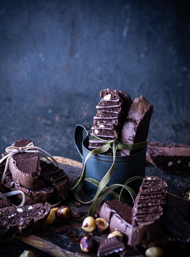 Black mug with chocolate hazelnut biscotti stacked inside with green bow tied around biscotti