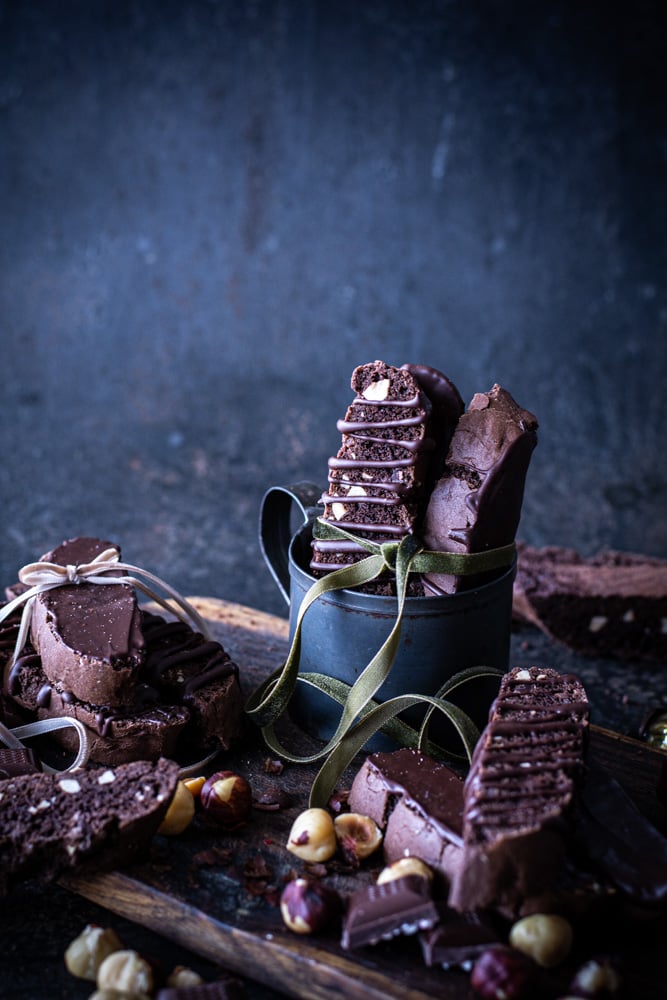 Black mug with chocolate hazelnut biscotti stacked inside with green bow tied around biscotti