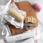 Marzipan on a cutting board sliced with two rolled up marzipan in white paper with red twine