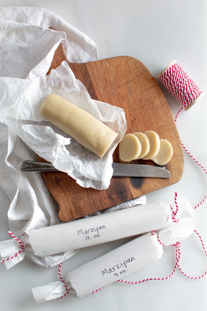 Marzipan on a cutting board sliced with two rolled up marzipan in white paper with red twine