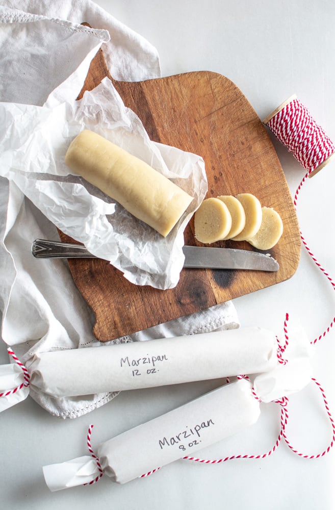 Marzipan on a cutting board sliced with two rolled up marzipan in white paper with red twine