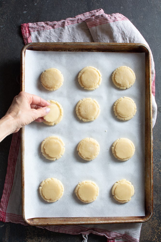 Hand placing disc of marzipan on top of sugar cookies