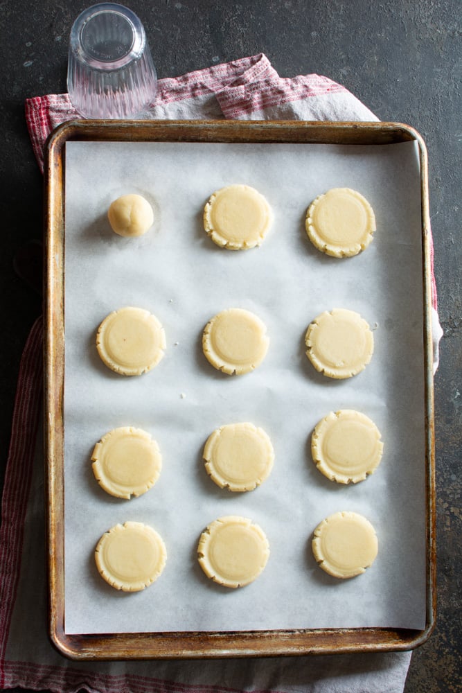 12 cookies on a baking sheet flattened with the bottom of a cup