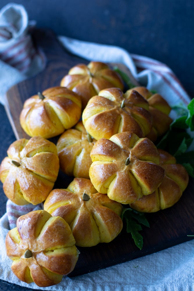 A dozen small pumpkin shaped rolls on a platter.