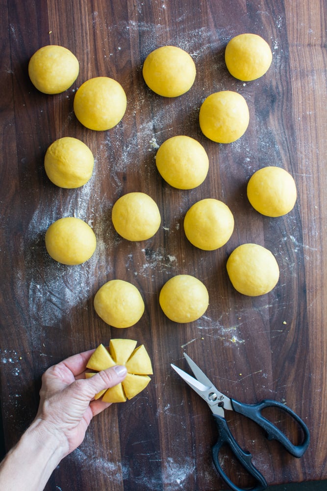 Round balls of pumpkin dough on a cutting board with one dough cut with 6 slits