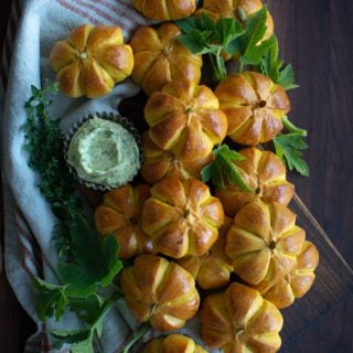 Arranged pumpkin buns on a cutting board with a bowl of herb butter