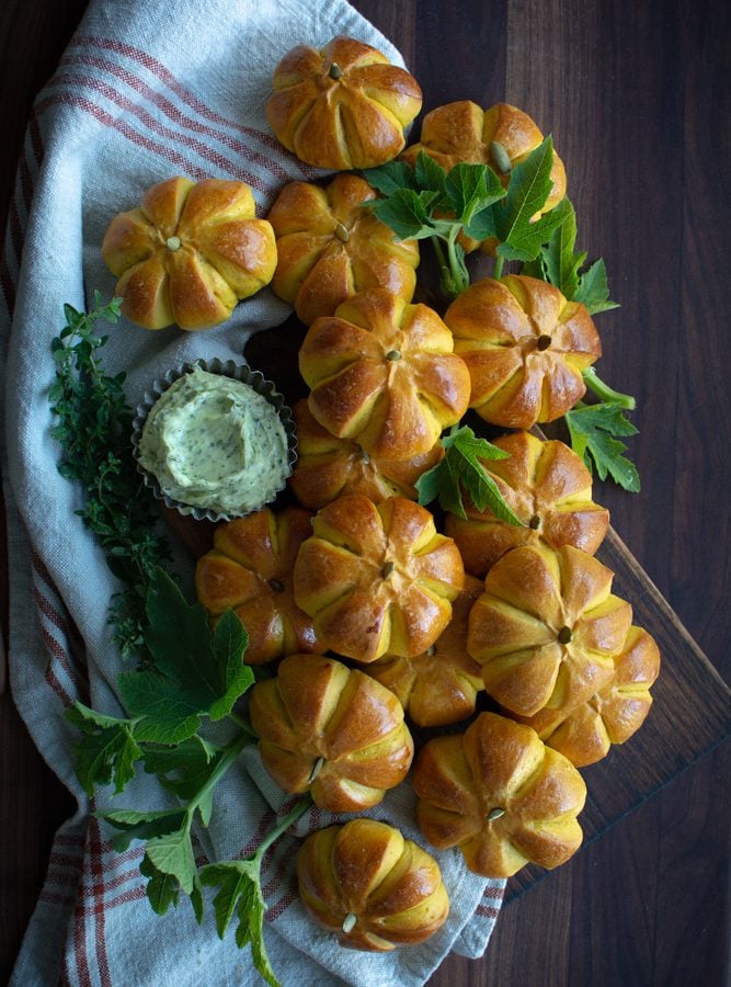 Arranged pumpkin buns on a cutting board with a bowl of herb butter