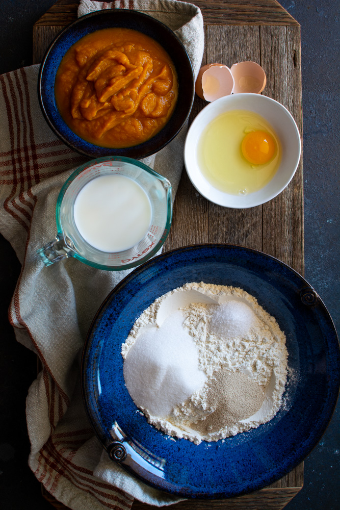 Large bowl with bun ingredients and bowls with pumpkin, milk, and butter