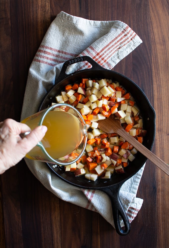 Chicken broth in measuring cup being poured over sautéed veggies