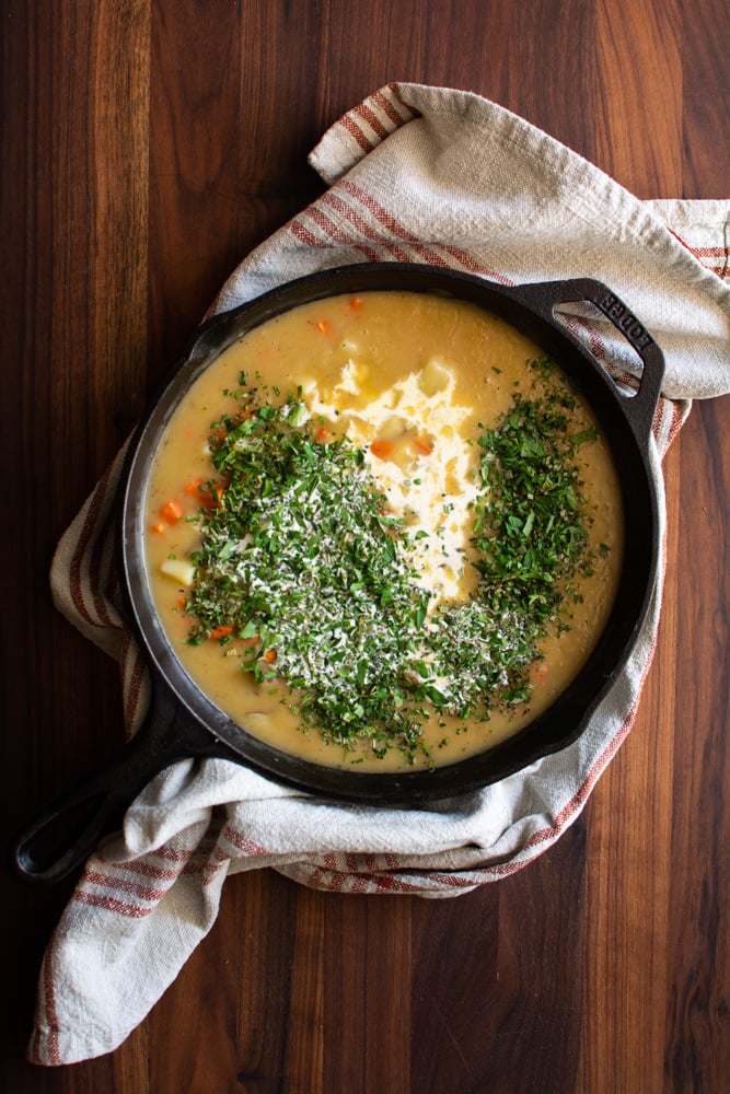 Chicken pot pie filling in a skillet with fresh herbs and cream on top.