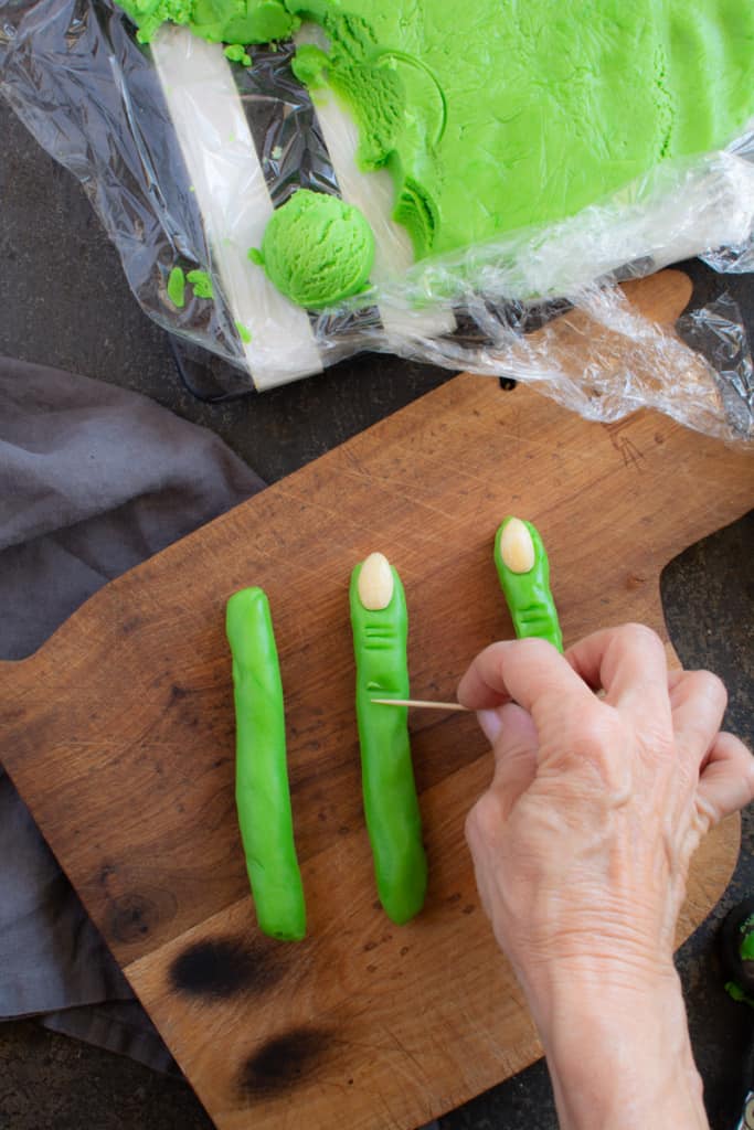 Hand with toothpick adding ridges to resemble knuckles across the cookies.