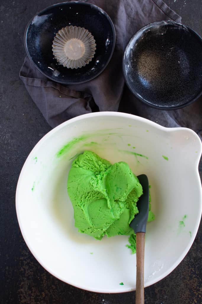 Bright green cookie dough mixed together in a white bowl, with spatula in the bowl to the side.