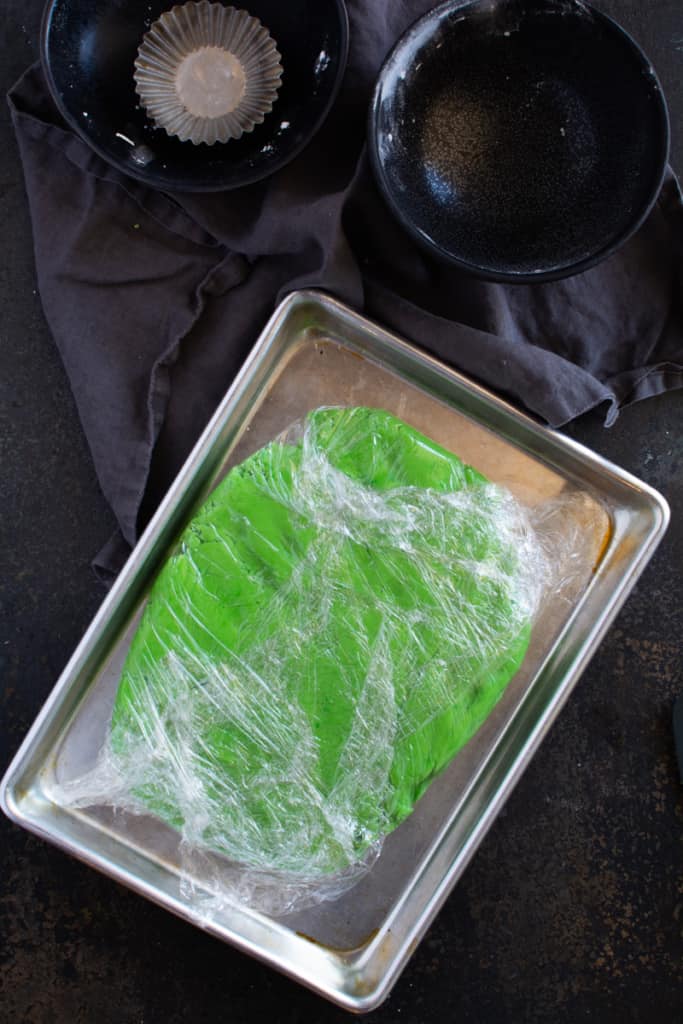 Green dough wrapped in plastic on a square baking sheet.