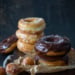 chocolate glazed and glazed spudnuts stacked on cutting board with donut holes