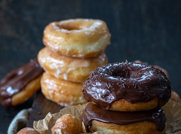 chocolate glazed and glazed spudnuts stacked on cutting board with donut holes