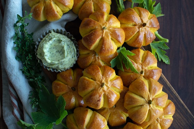 Arranged pumpkin buns on a cutting board with a bowl of herb butter