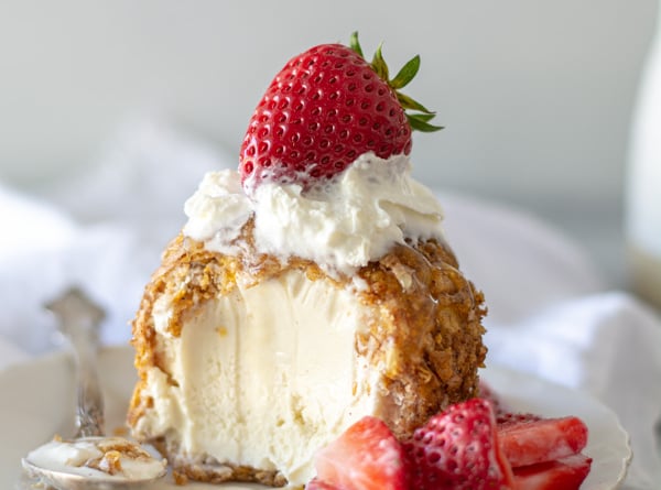 fried ice cream with spoonful taken out with honey and berries